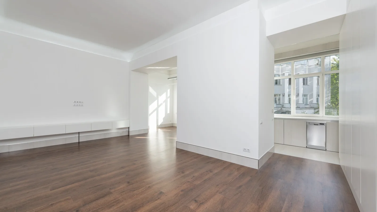 A bright, empty rented apartment with bare white walls and wooden floors on move-in day