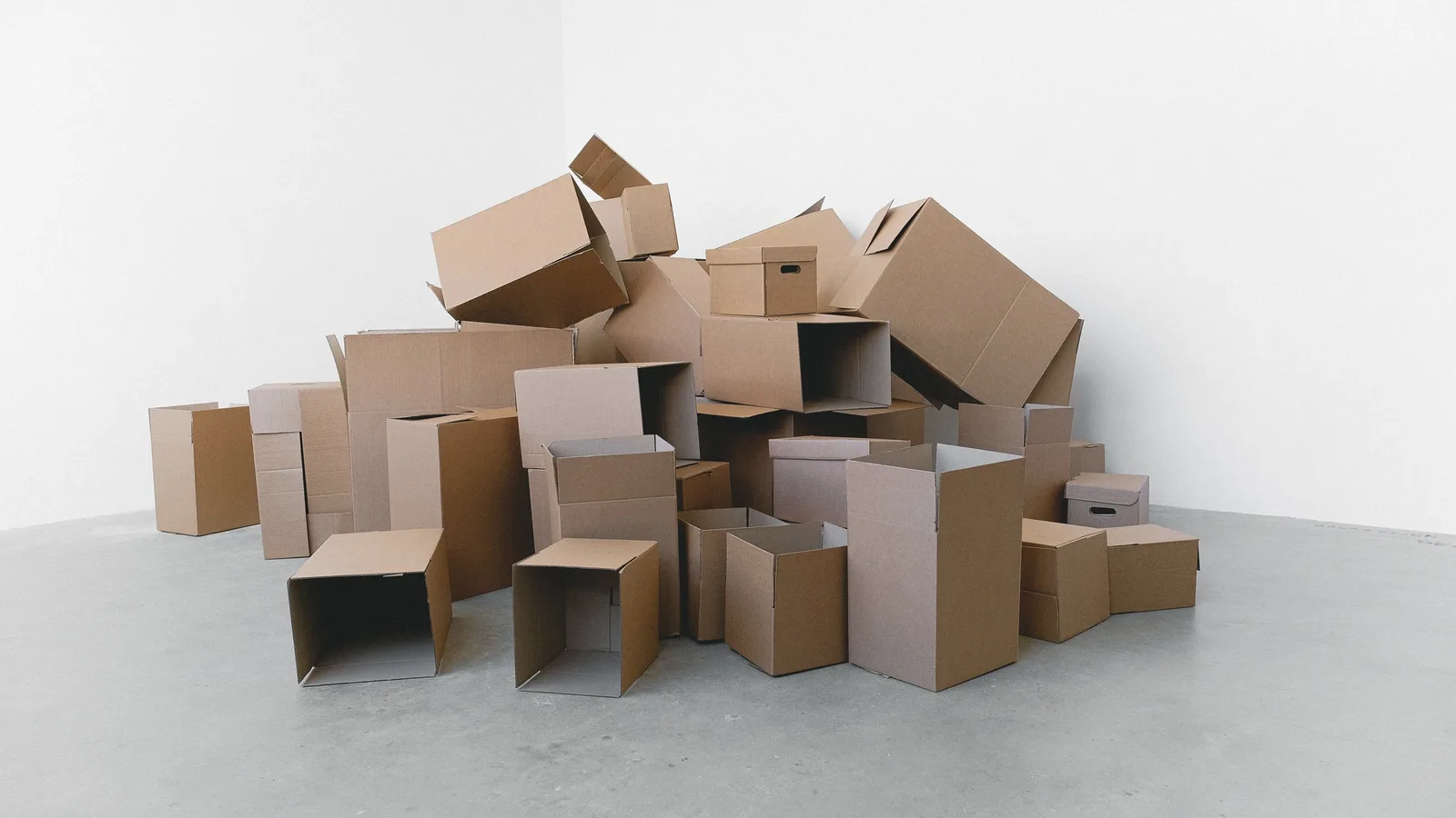 A large pile of unlabelled cardboard moving boxes stacked in a bare room