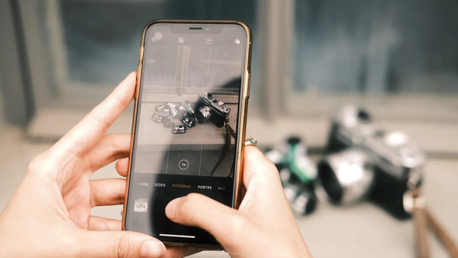 Someone holding a phone to photograph a camera and rolls of film laid out on a table